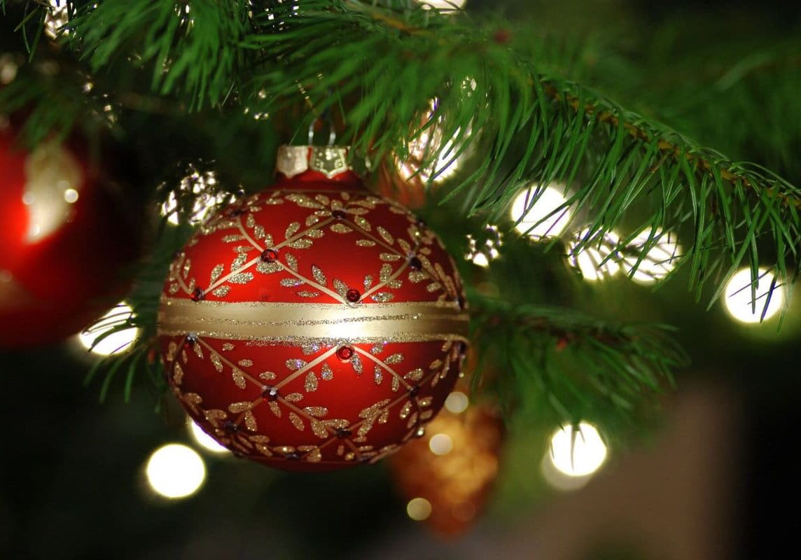 A red and gold ornament hanging from the side of a christmas tree.