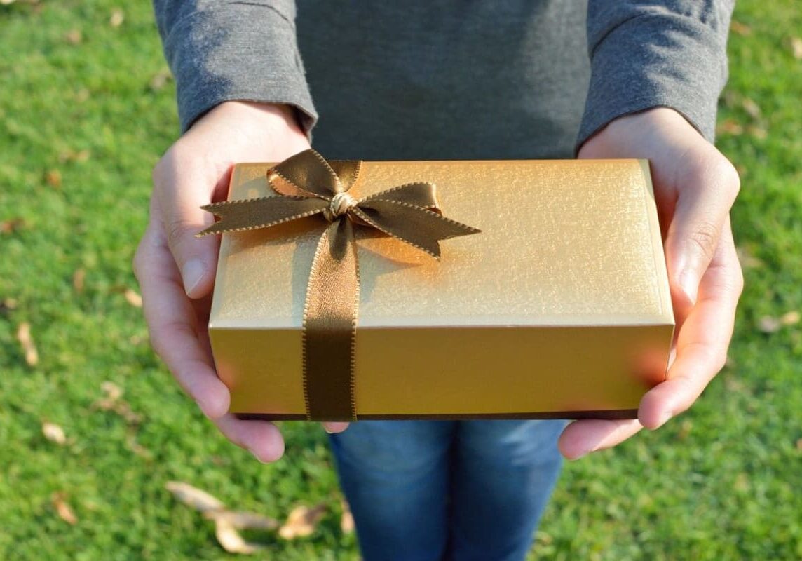 A person holding a gold gift box in their hands.